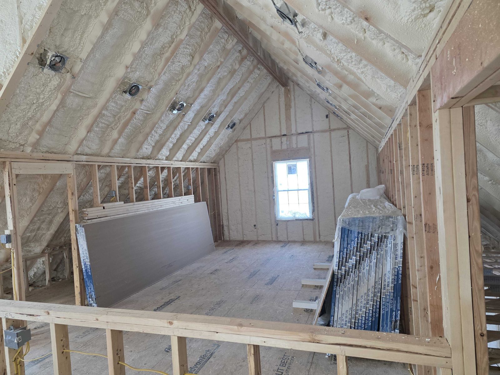 An upper level room framed with a window opening, prepped for spray foam.